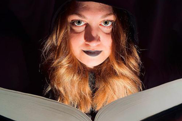 Foto af kvinde, der kigger i en bog, og belyses nedefra, så hun ser uhyggelig ud.
